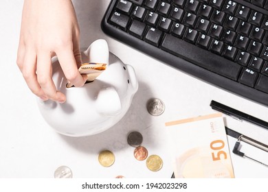 Child Puts Money Into The Piggy Bank On White Background With Clipboard, Coins And Keyboard, Long Banner Format. Financial Education For Children Concept.