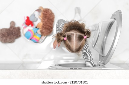 The Child Puts Toys In The Washing Machine. View From Above.