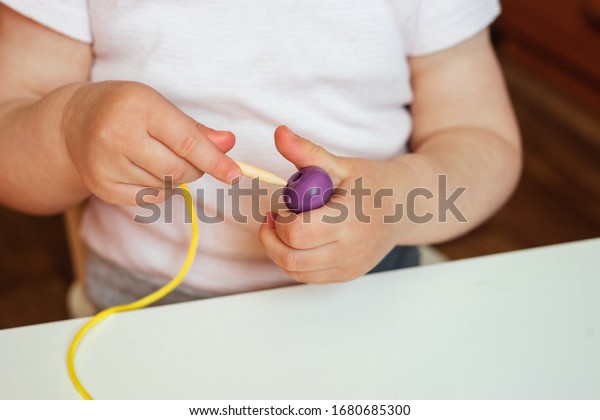 Child putting beads on a string. Bead stringing
activity. Fine motor skills development. Early education,
Montessori Method. Cognitive skills, children development. Close up
of baby's hands.