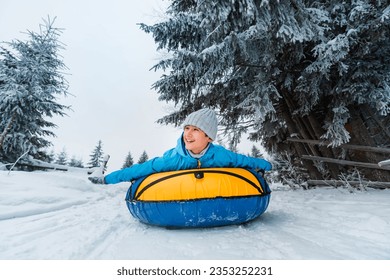 Child races down snowy slope on tubing. Inflatable sleds for active winter recreation. Beautiful snowy winter forest background.