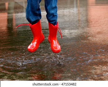 Child With Rain Boots Jumps Into A Puddle