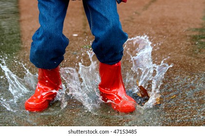 Child With Rain Boots Jumps Into A Puddle