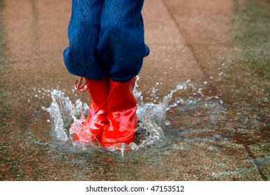 Child With Rain Boots Jumps Into A Puddle