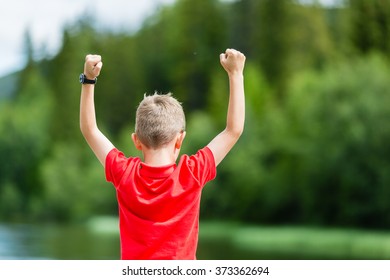 Child with raised arms celebrating his success or victory while standing outdoors.