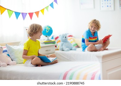 Child Reading Book In Bed. Bedroom For Two Kids. Little Boys Read Books On White Bed With Colorful Bedding. Children Nursery. Kid Boy Siblings Play Indoors. Nap And Sleep Time. Student Doing Homework.