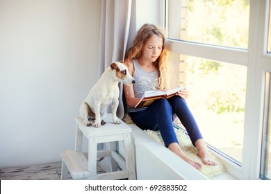 Child Reading Book At Home. Girl Sitting At Window At Read