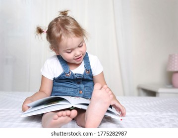 Child Reading A Book Indoors.Caucasian Kid Reads A Book Sitting On A Bed.Night Fairy Tail.Preschool Girl Holding A Book And Learns To Read.