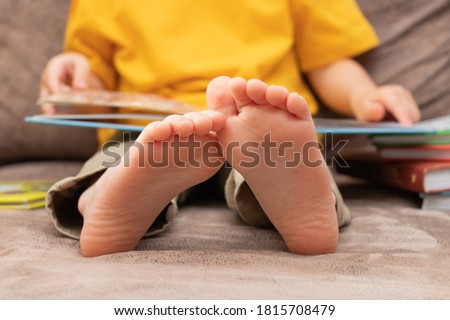 The child is reading a book on the sofa, feet close up. Childhood and education conception.
