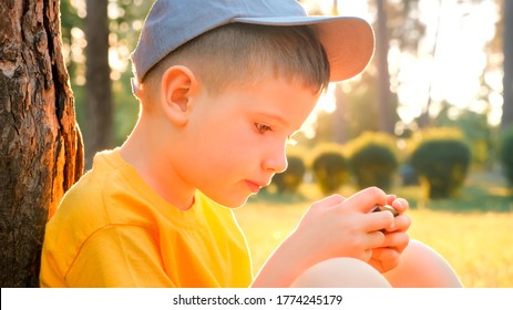 Child reading ebook on mobile outdoor. Kid with gadget in park, garden. Boy in cap playing game on smartphone. Elearning, education online. Preschooler spends time on fresh air. Pediatrics, psychology