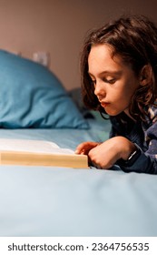 child reads a book before going to bed. Children's book to read in bed. Children read books. Children's room. Little curly boy in pajamas at home. - Shutterstock ID 2364756535