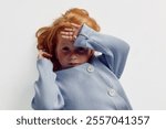 Child with red hair laying on floor with hands on head in playful pose of innocence and wonder