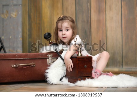A child in a retro interior and an old phone sits on the floor. A small child a traveler in vintage decorations. Child traveler is calling by phone.
