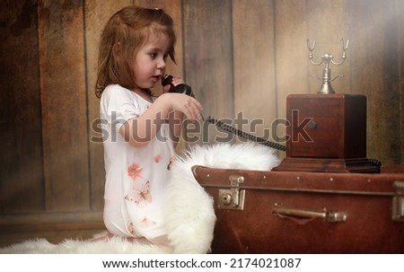A child in a retro interior and an old phone sits on the floor. A small child a traveler in vintage decorations. Child traveler is calling by phone.

