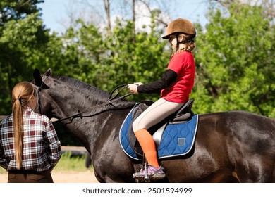 Child rider adjusts position on horse under instructor's watch. Riding school - Powered by Shutterstock