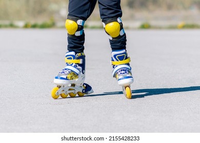 A child rides blue yellow and white roller skates. Cropped shot of a little boy learning to rollerblade on asphalt. Active leisure. Sunny summer day
