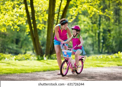 Child Riding Bike. Kid On Bicycle In Sunny Park. Mother Teaching Little Girl To Cycle. Preschooler Learning To Balance Wearing Safe Helmet. Sport For Parents And Kids. Family Outdoor On Bike Ride