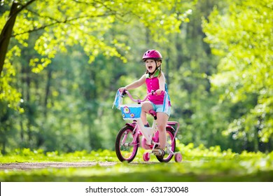 Child Riding Bike. Kid On Bicycle In Sunny Park. Little Girl Enjoying Bike Ride On Her Way To School On Warm Summer Day. Preschooler Learning To Balance On Bicycle In Safe Helmet. Sport For Kids