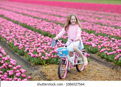 Child Riding Bike In Tulip Flower Field During Family Spring Vacation In Holland. Kid Cycling In Pink Tulips. Little Girl Cycling In The Netherlands. European Trip With Kids. Travel With Children.