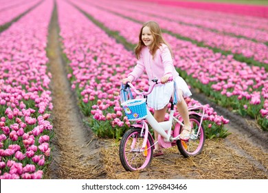 Child Riding Bike In Tulip Flower Field During Family Spring Vacation In Holland. Kid Cycling In Pink Tulips. Little Girl Cycling In The Netherlands. European Trip With Kids. Travel With Children.