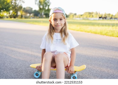 Child Riding Skateboard In Summer Park. Little Girl Learning To Ride Skate Board. Active Outdoor Sport For School And Kindergarten Kids. Children Skateboarding. Preschooler Sitting On Skateboard.