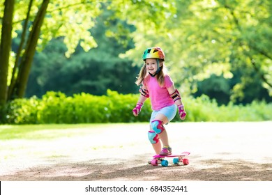 Child Riding Skateboard In Summer Park. Little Girl Learning To Ride Skate Board. Active Outdoor Sport For School And Kindergarten Kids. Children Skateboarding. Preschooler On Longboard. Kid Skating.