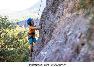 Child Rock Climber. The Boy Climbs The Rock. The Child Is Engaged In Rock Climbing On Natural Terrain. Sports Kid Spends Time Actively. Do Outdoor Sports.