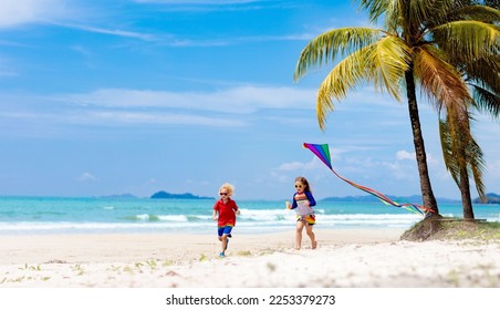 Child running with colorful kite on tropical beach. Kid flying rainbow kite. Little girl playing with toy airplane on sea shore. Family summer vacation on exotic island. Water and sand fun for kids. 