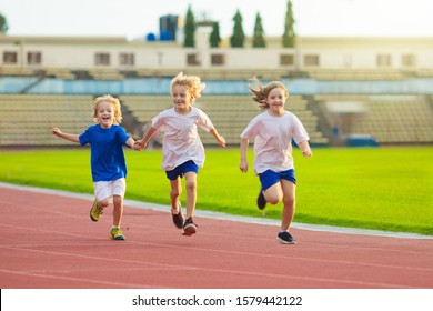 Child Running In Stadium. Kids Run On Outdoor Track. Healthy Sport Activity For Children. Little Girl And Boy At Athletics Competition Race. Young Athlete In Training. Runner Exercising. 