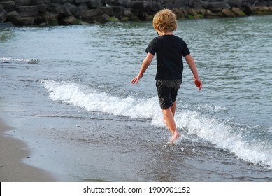 Child Running In Water Along Shore Of Beach Fully Clothed