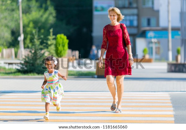 The\
child runs away from the mother on the pedestrian crossing. A black\
girl runs along the road from her mother, a\
danger.