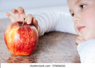 A Child Sad Looks On The Red Ripe  Apple  On The Brown Surface Of Marble, Poor Appetite