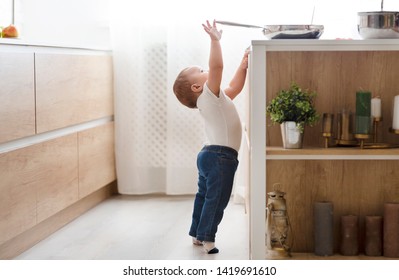 Child safety at home concept. Little baby reaching for hot pan on stove in kitchen, empty space