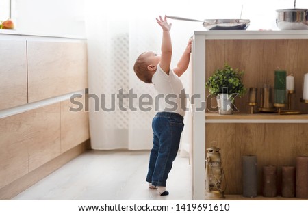 Child safety at home concept. Little baby reaching for hot pan on stove in kitchen, empty space