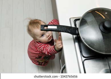 child safety at home concept - toddler reaching for pan on the stove in kitchen