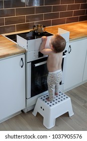 Child Safety At The Stove. A Little Baby Child Is Curious And Tries To Take A Hot Pot On A Stove.