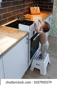 Child Safety At The Stove. A Little Baby Child Is Curious And Tries To Take A Hot Pot On A Stove.