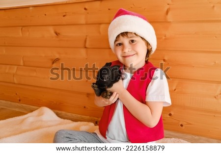 Child in Santa Claus costume hugs with black rabbit. Boy stroke domestic animals. Zoo therapy with furry pets. Merry Christmas and happy New Year. Hare is the symbol of 2023 by the Chinese calendar. Stock photo © 