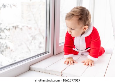 Child In Santa Suit On The Sill Of The Window, The Concept Of New Year And Christmas