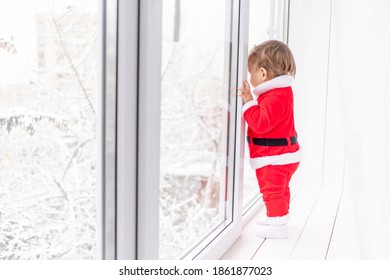 Child In Santa Suit On The Sill Of The Window, The Concept Of New Year And Christmas