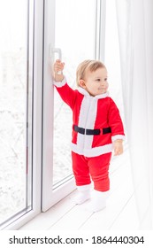 Child In Santa Suit On The Sill Of The Window, The Concept Of New Year And Christmas