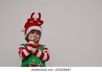 Child in Santa's hat, hand near face, Christmas waiting pose. Isolate on white, space for text - Shutterstock ID 2233330667