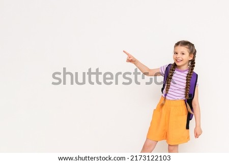A child with a satchel points with his index finger at your advertisement on a white isolated background. Preparatory summer courses for children. Copy space.