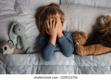 The child was scared before going to bed. Night terrors in a child. The kid covers his face with his hands in a fear. Children's experiences. Boy in the bed. View from above. Sad psychological state. - Shutterstock ID 2109215756