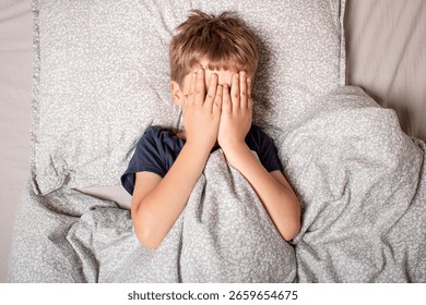 The child was scared before going to bed. Night terrors in a child. The kid covers his face with his hands in a fear. Children's experiences. Sad psychological state. Nightmares or fear of darkness.