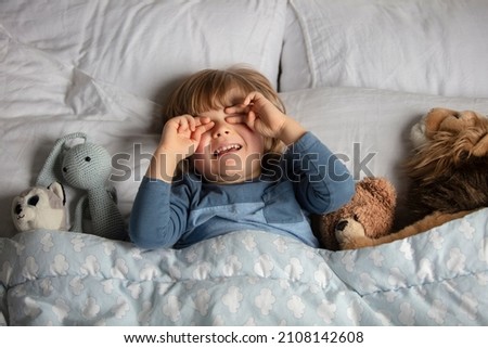 The child was scared before going to bed. Night terrors in a child. The kid covers his face with his hands in a fear. Children's experiences. Boy in the bed. View from above. Sad psychological state.