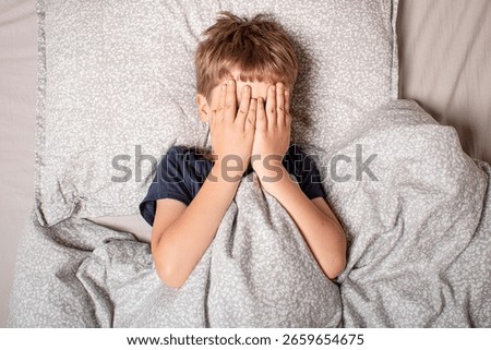 The child was scared before going to bed. Night terrors in a child. The kid covers his face with his hands in a fear. Children's experiences. Sad psychological state. Nightmares or fear of darkness.