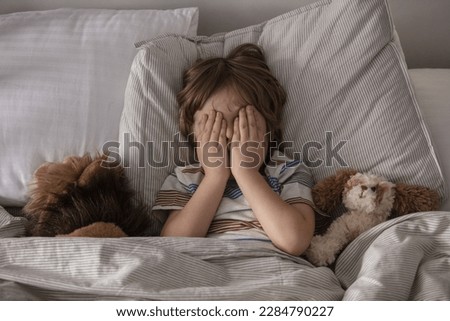 The child was scared. Night terrors in a child. The kid covers his face with his hands in a fear. Children's experiences. Boy in the bed. View from above. Sad psychological state.