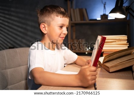 child schoolboy doing homework at night at home, boy reading book preparing for exam late evening, home learning concept