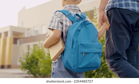 Child Schoolboy walking down street with backpack, holding his dad by hand. Happy family, father, child go to school together. Dad is taking his little son with textbook to school. Preschool education - Powered by Shutterstock