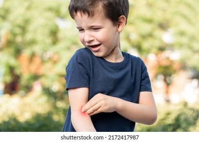 Child Scratching Arm Because It Stings In A Park With A Green Background